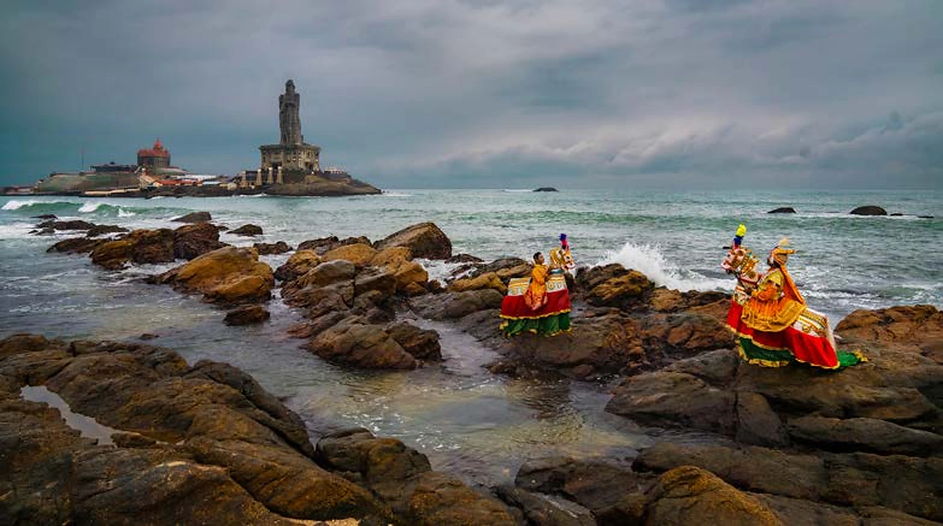 Performers in vivid traditional dress photographed on a rocky shoreline