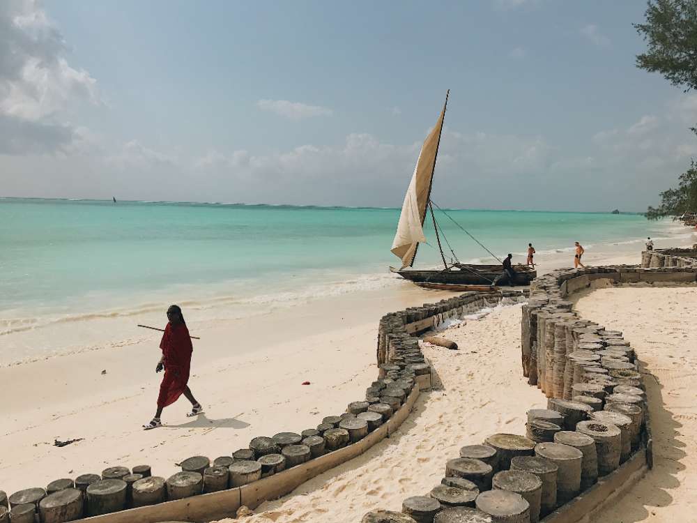 A dhow pulled up on the beach in Zanzibar, a man walking past in red