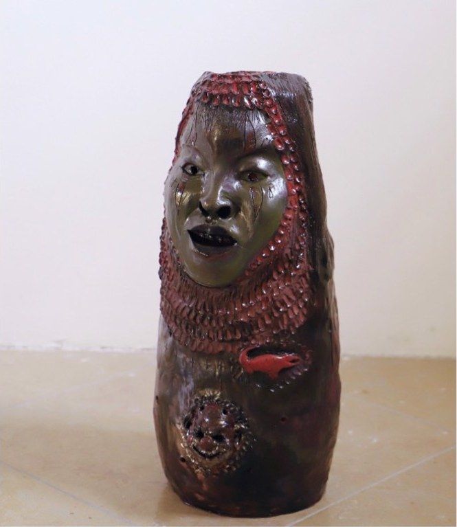 A ceramic vessel with a modelled face and red beaded surface