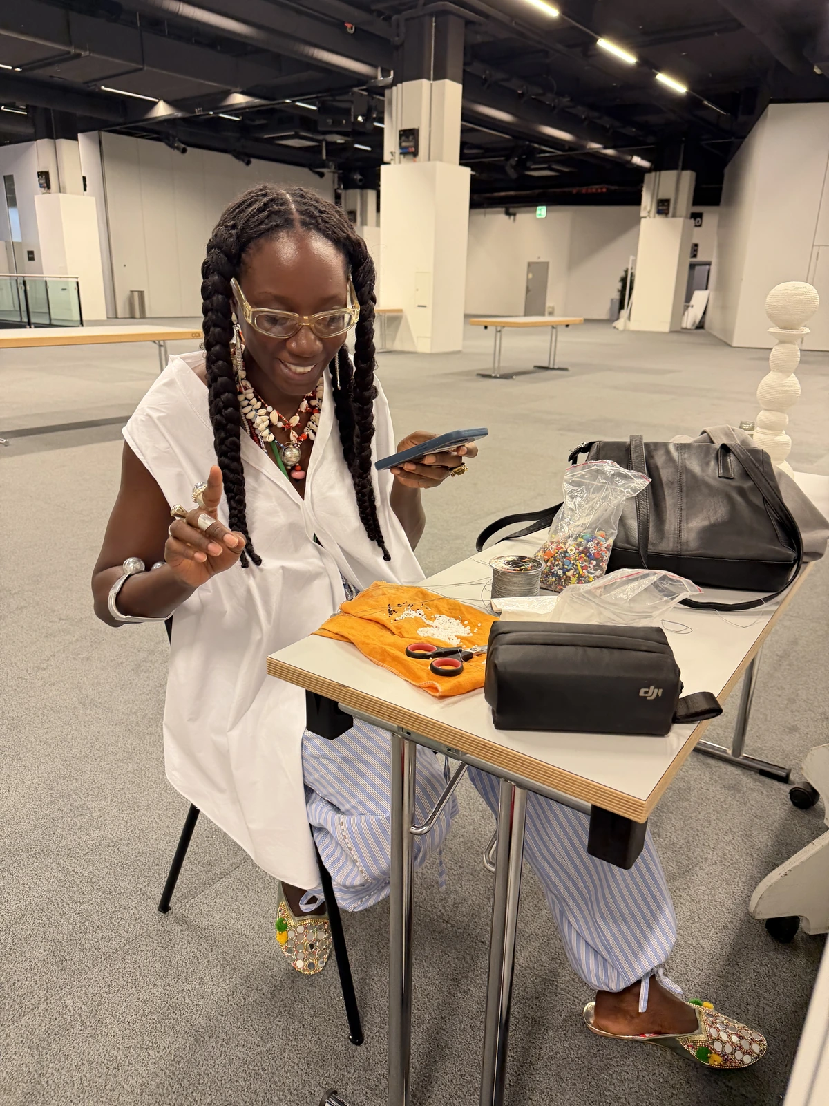 Luma Nascimento at the work table with beads, a spool of wire and small silver components laid out on an orange cloth