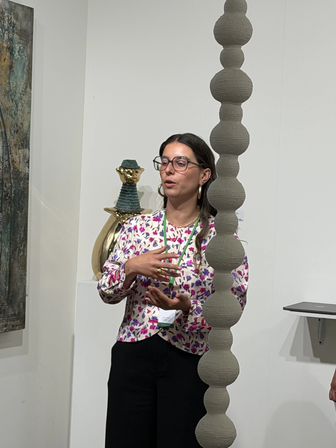 A gallery walkthrough at the booth, a speaker gesturing towards a tall hanging column of stacked spheres while visitors listen