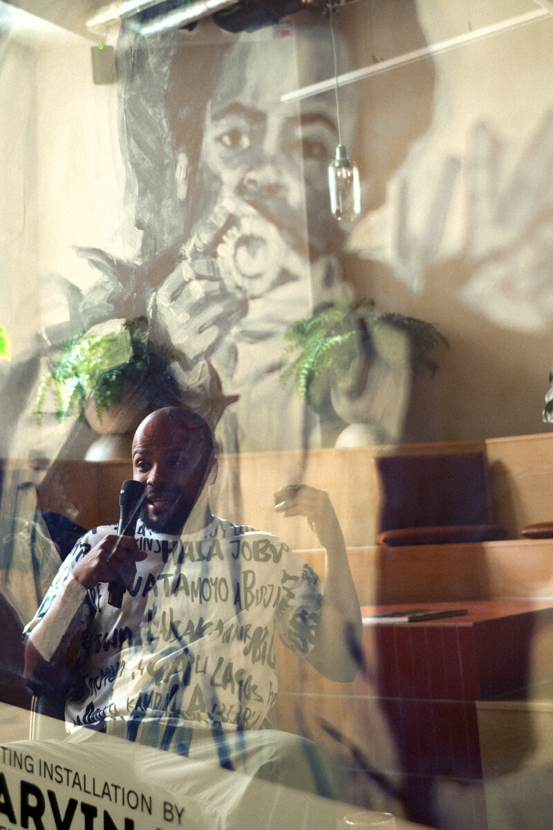 Marvin Kangsen speaking, reflected against his painting from the Slice of the Cake poster